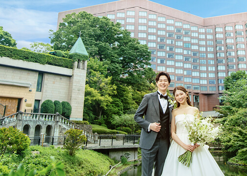 ホテルの庭園で青空を背景に笑顔で寄り添う新郎新婦