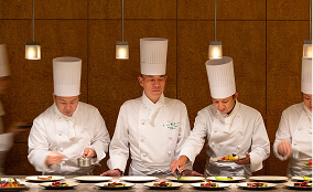 白いコック帽をかぶったシェフたちが料理を準備している厨房の様子