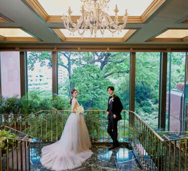 大きな窓から庭園の緑を望む階段に立つ新郎新婦