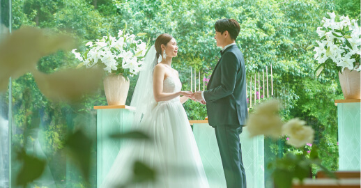 緑に囲まれたテラスで手を繋ぎ見つめ合う新郎新婦