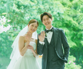 緑あふれる屋外で手を取り合い笑顔を見せる新郎新婦