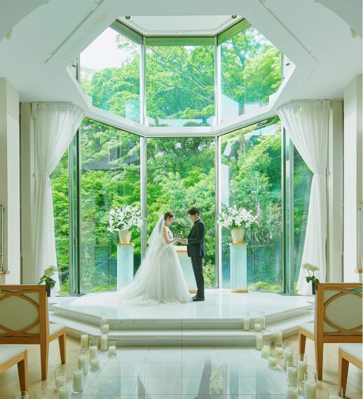 大きな窓から自然光が差し込む白いチャペルで挙式を行う新郎新婦