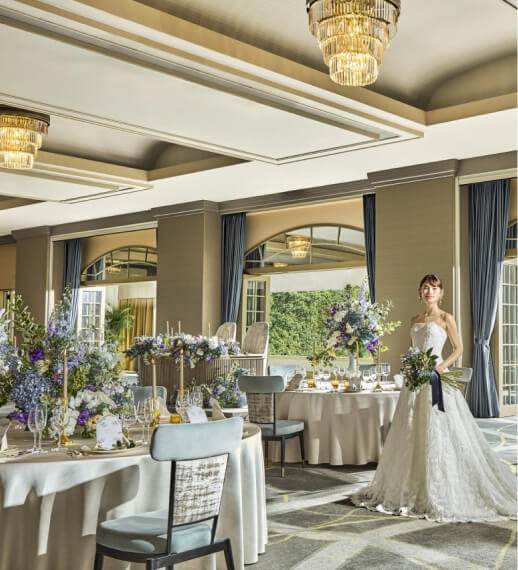 豪華なシャンデリアと格子天井の披露宴会場で紫の花装飾とテーブルセッティングの中に立つ花嫁