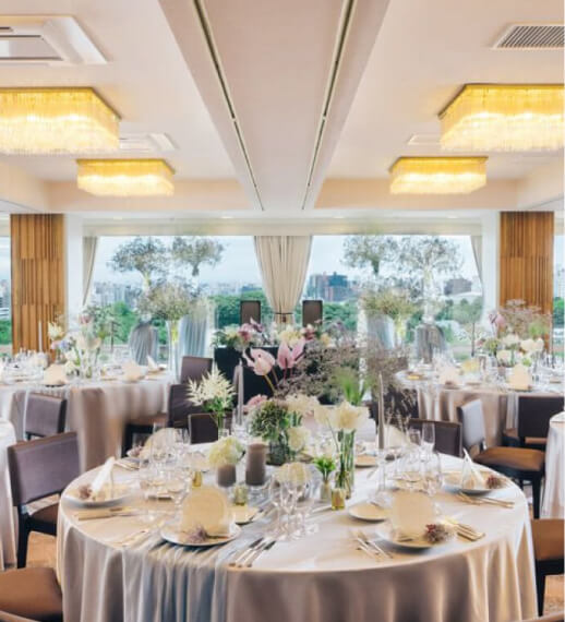 都市の景色を一望できる高層階の披露宴会場、丸テーブルと上品な花装飾が配置された空間